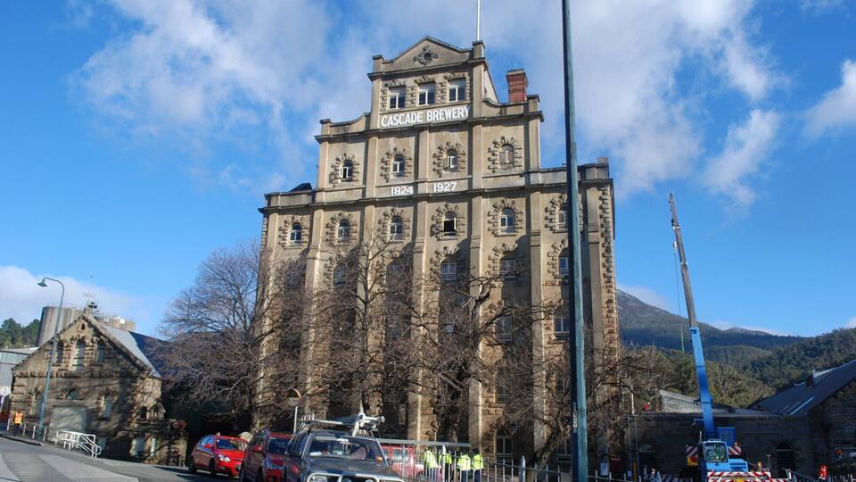 Cascade Brewery with a sign indicating its establishment years 1824 and 1927, surrounded by trees and parked cars.