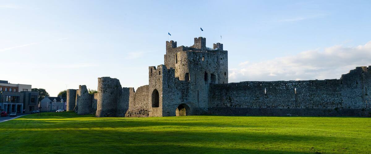 A historic castle with a large grassy courtyard, multiple towers, and flags.