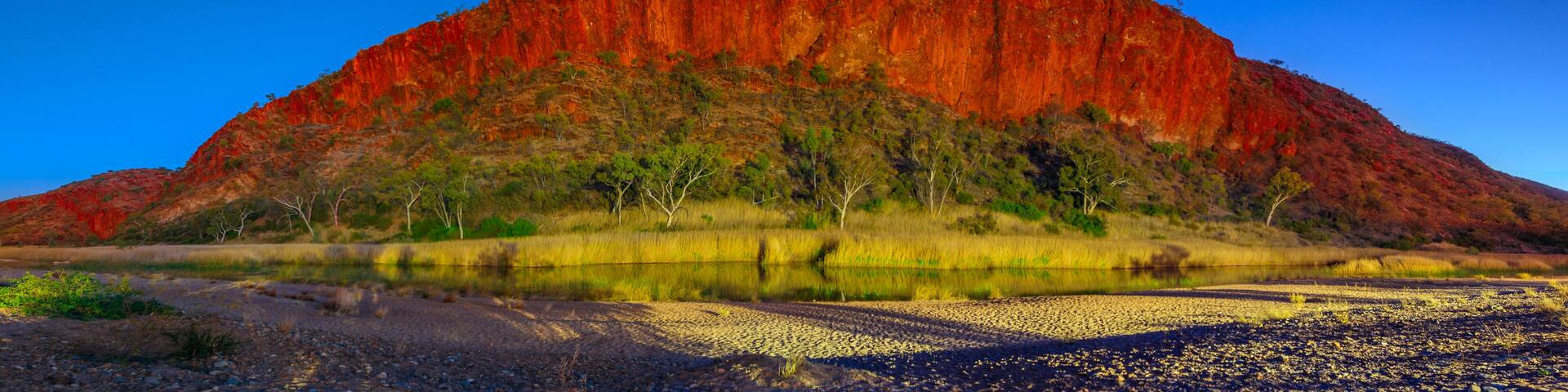A large red rock formation with a river in the foreground.