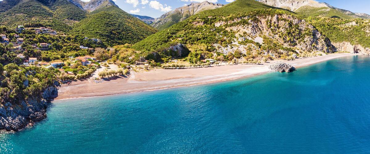 A coastal town with a beach, clear blue waters, and green hills.