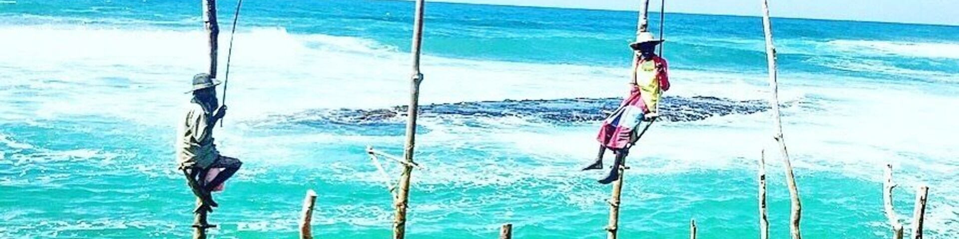 Uma praia rochosa com estacas de bambu e uma pessoa em cima de uma delas.