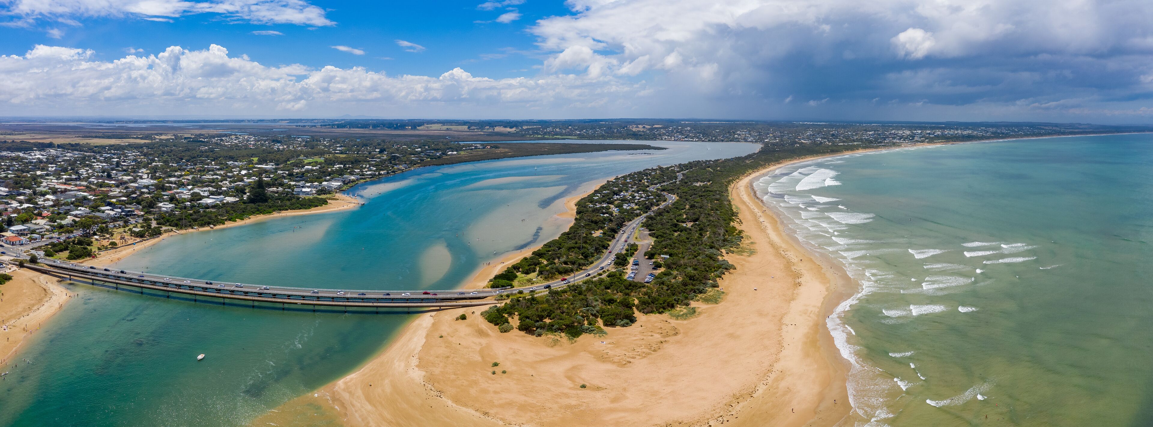 An aerial view of a coastal town with a bridge, beaches, and a bay.