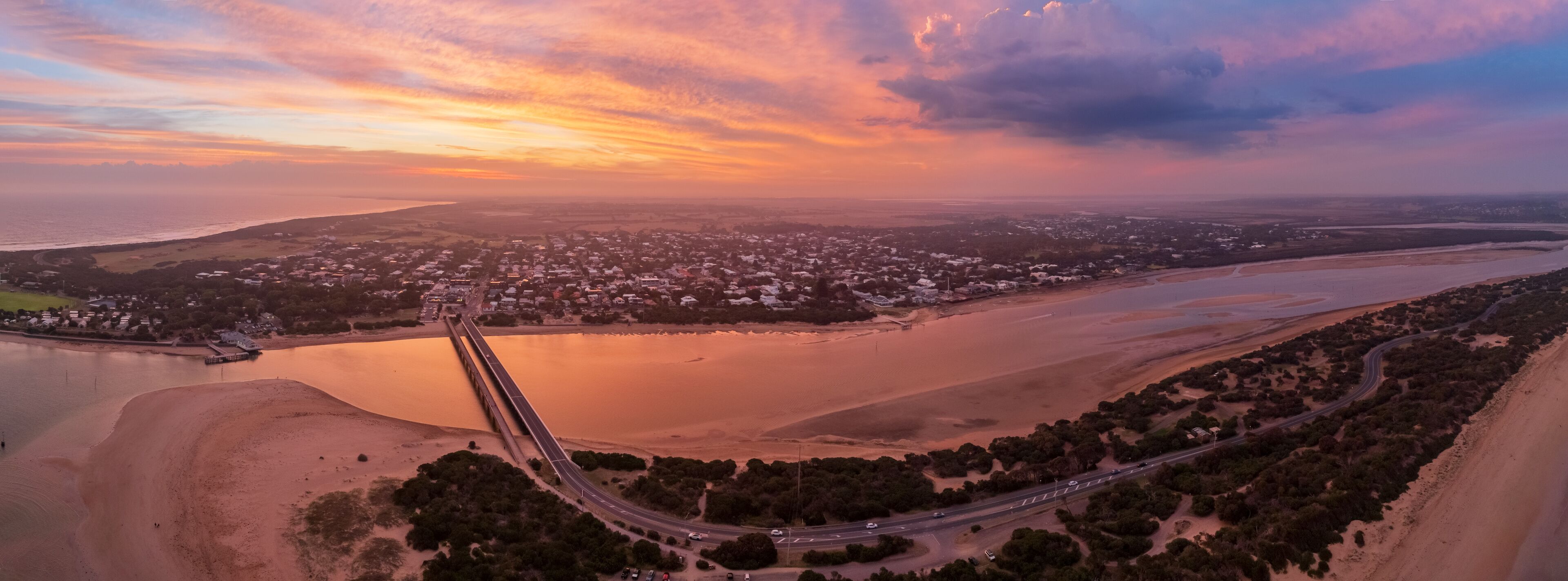 An aerial view of a coastal city with a bridge, roads, and a large body of water.