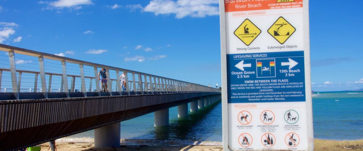 Señal de playa con advertencias e información sobre servicios de salvamento.