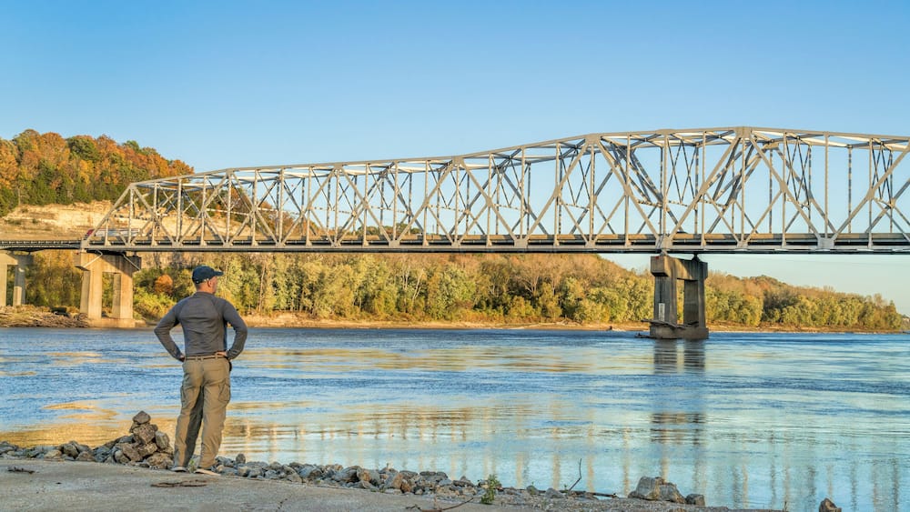Lonely male figure at the old boat ramp on Missouri River at Taylor's Landing near Rocheport, MO, fall colors scenery with the bridge view