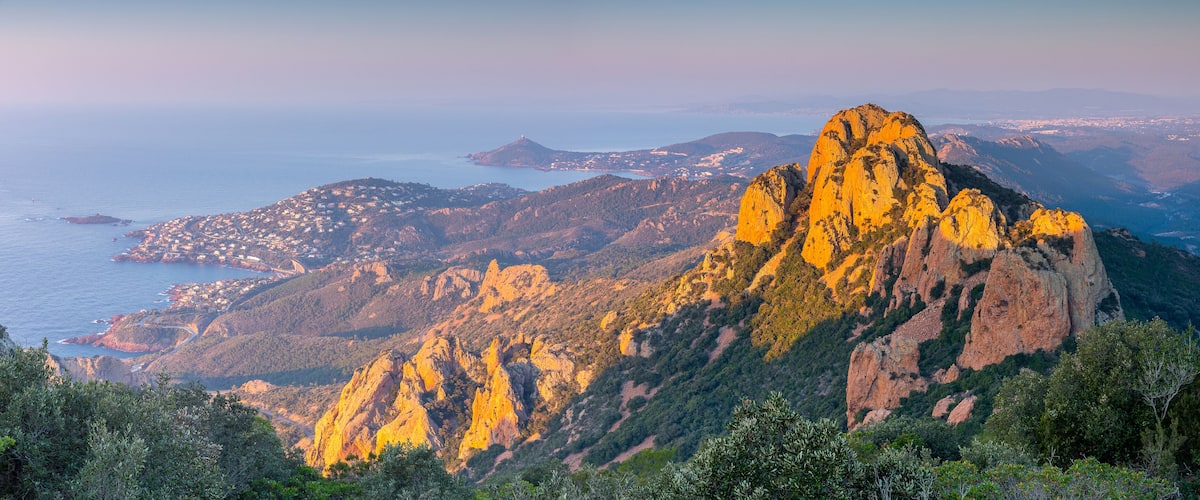 A mountainous landscape with a prominent rocky peak, coastal town, and distant islands.