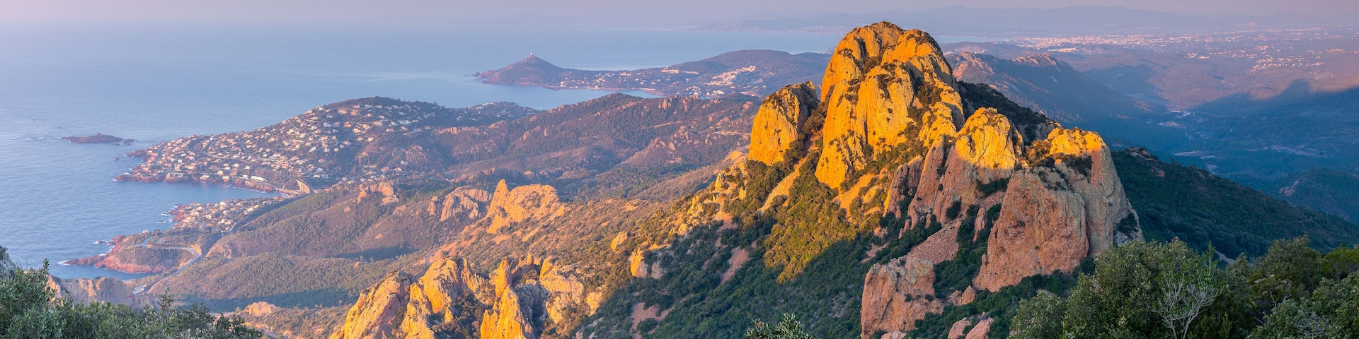 A mountainous landscape with a prominent rocky peak, coastal town, and distant islands.