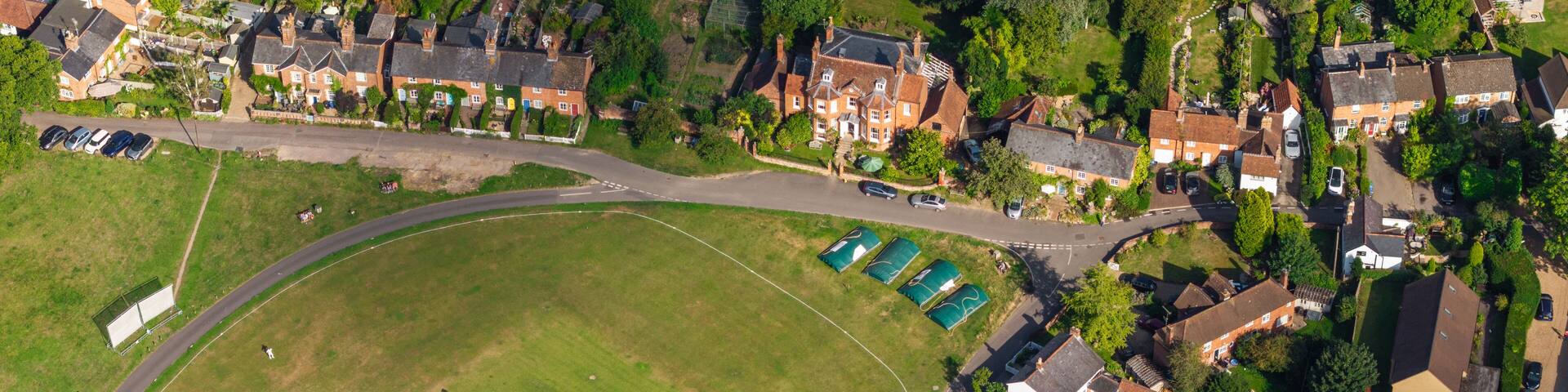 Aerial view of a vibrant green cricket field contrasting with the brick rooftops and lush trees, creating a picturesque scene, Hook, England, United Kingdom.