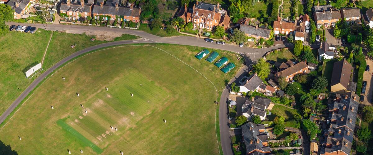 An aerial view of a residential area with houses, a large green field, and a sports field.