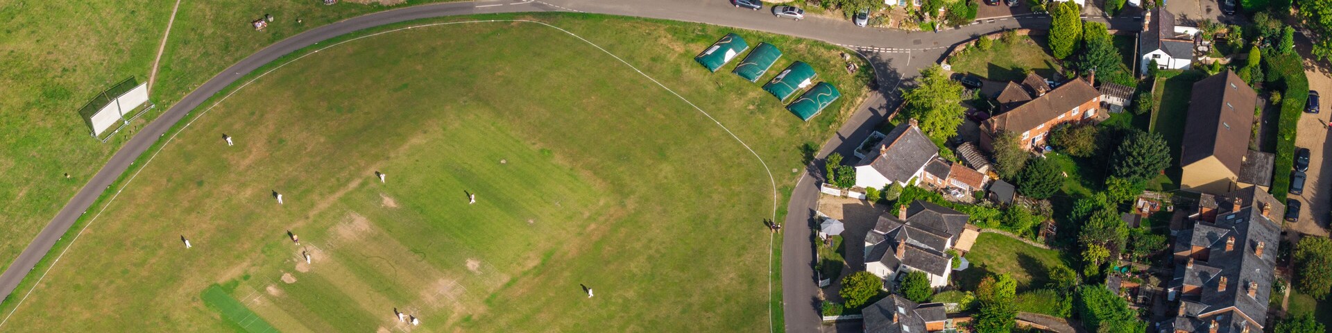 An aerial view of a residential area with houses, a large green field, and a sports field.