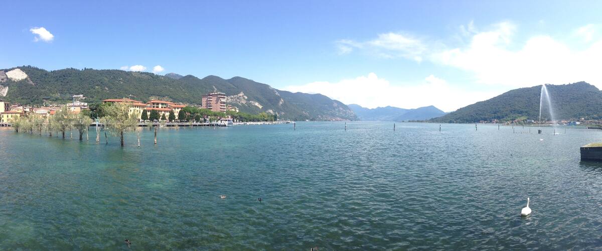 A calm lake with clear water, surrounded by mountains and buildings.