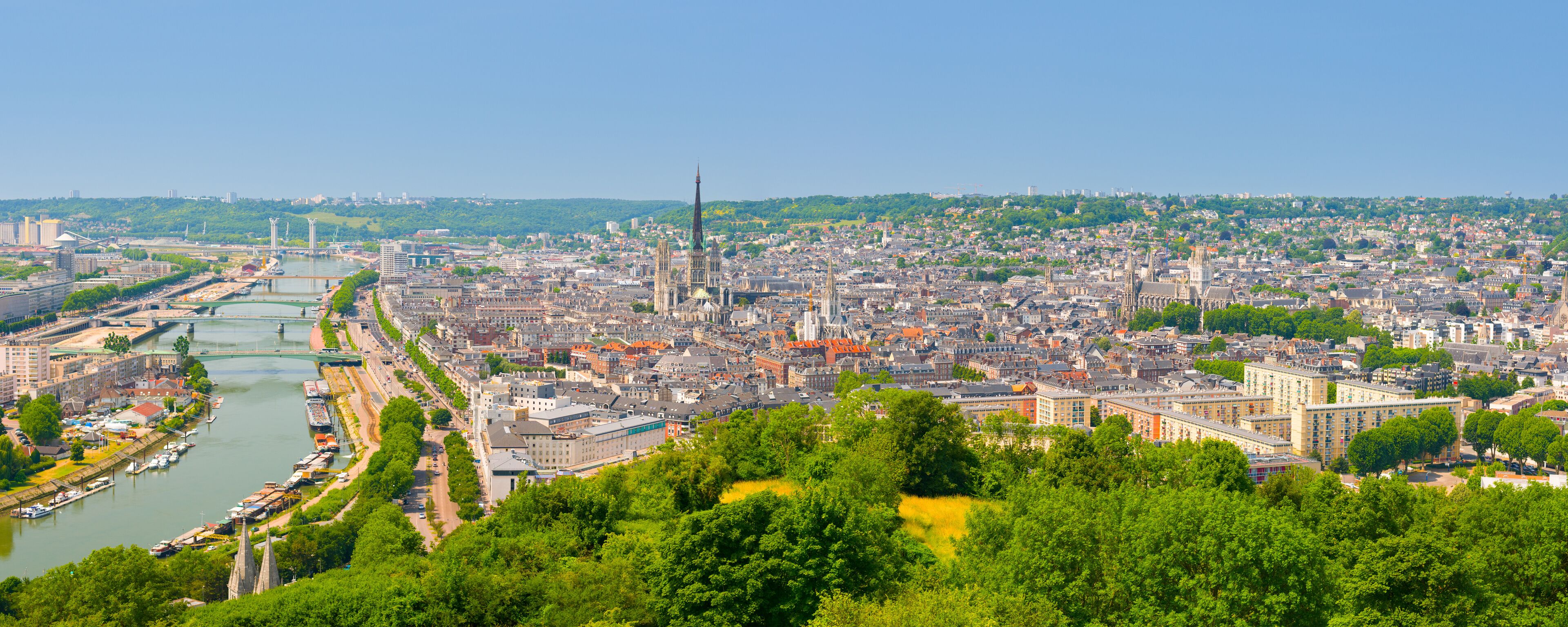 A panoramic view of a city with a river, green hills in the background, and historic buildings.