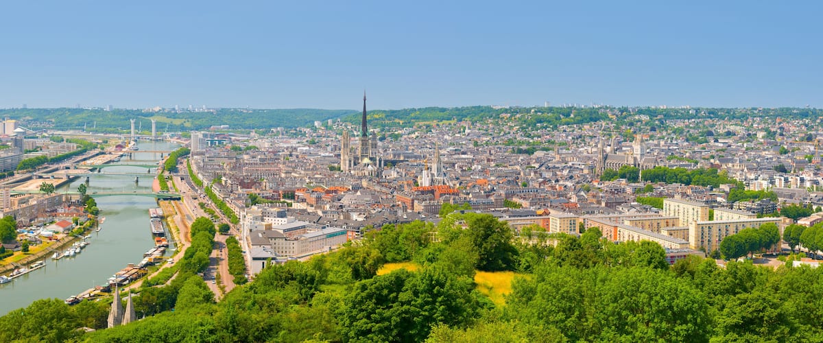 A panoramic view of a city with a river, green hills in the background, and historic buildings.