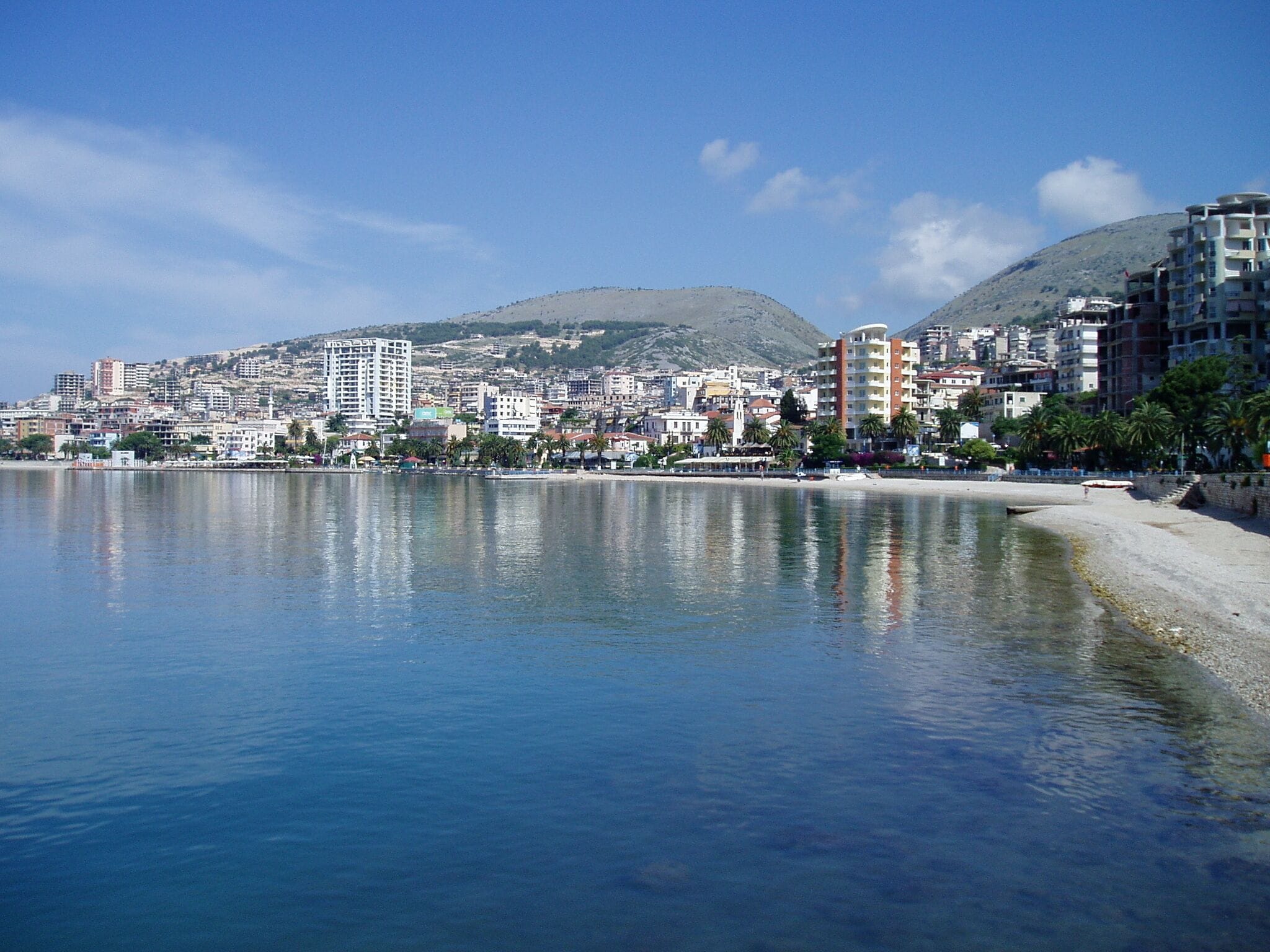 A coastal cityscape with a beach, buildings, and a mountain in the background.