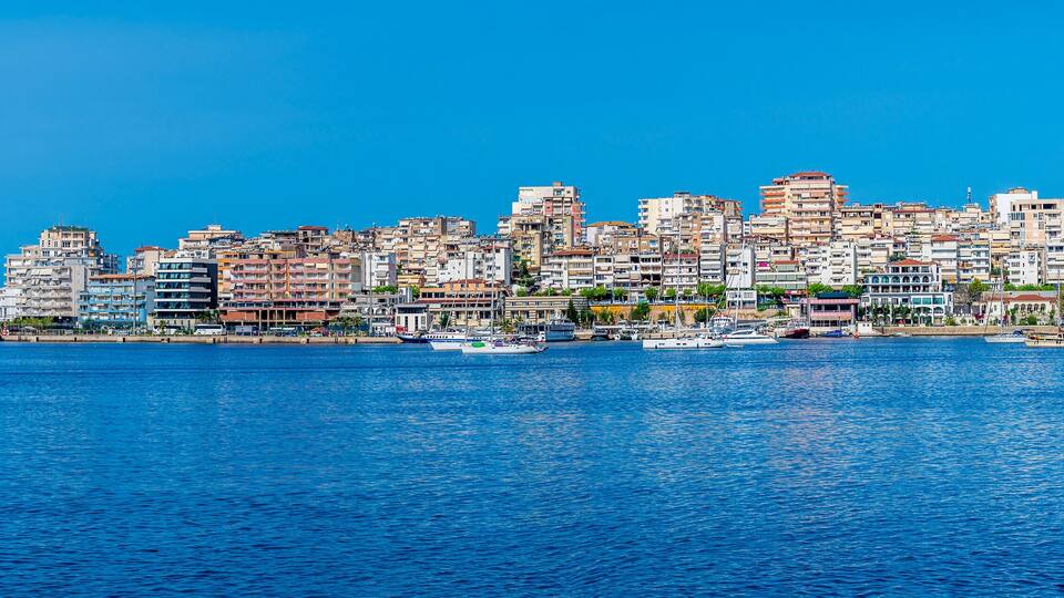 A coastal cityscape with densely packed buildings and a marina with several boats.