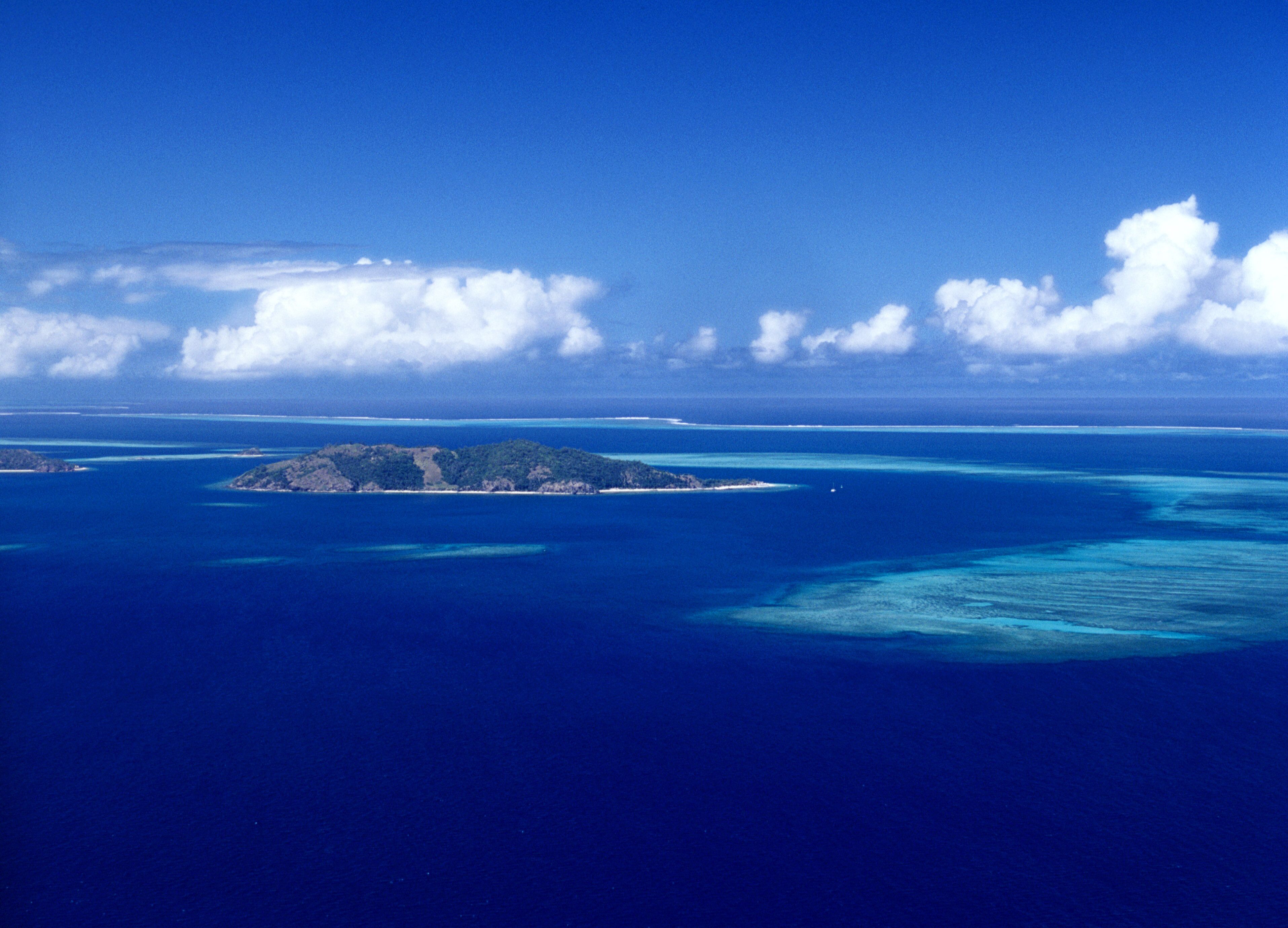 A tropical island surrounded by clear blue waters and a few scattered clouds.