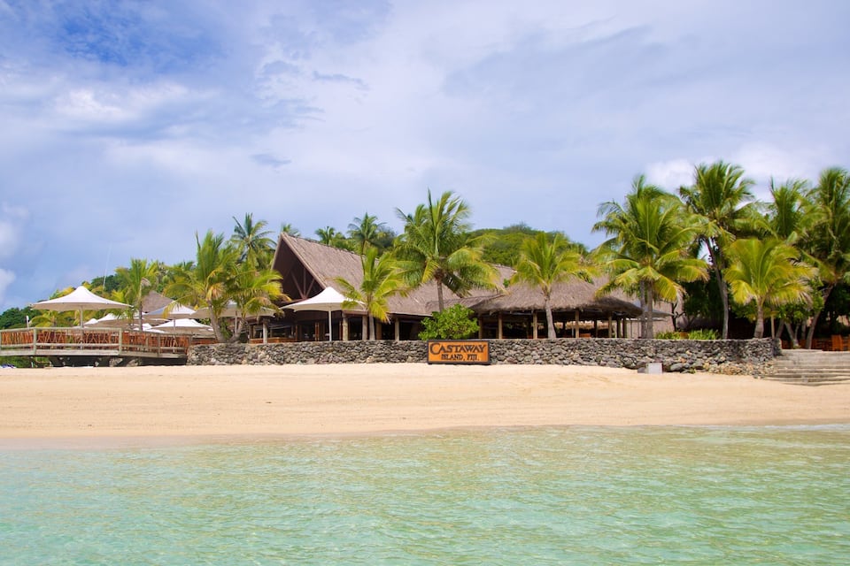 Un resort en la playa con edificios de techo de paja, palmeras y agua turquesa cristalina.