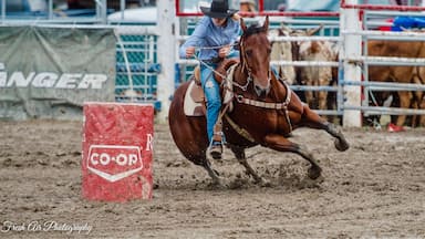 A person riding a horse in a rodeo arena with a red barrel labeled "CO-OP".