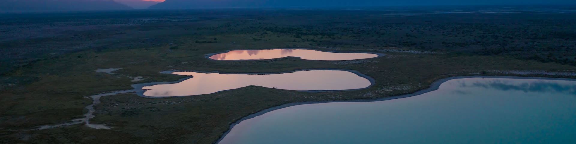 A sunset over a desert landscape with multiple water bodies and distant mountains.
