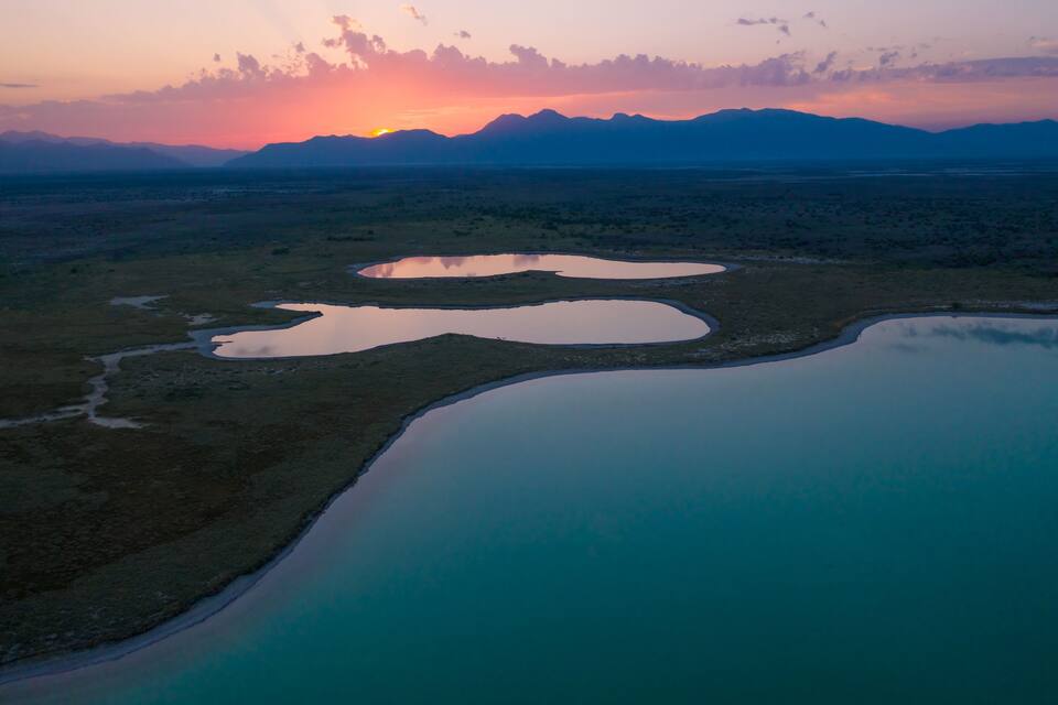 Atardecer sobre un paisaje desértico con varias masas de agua y montañas distantes.