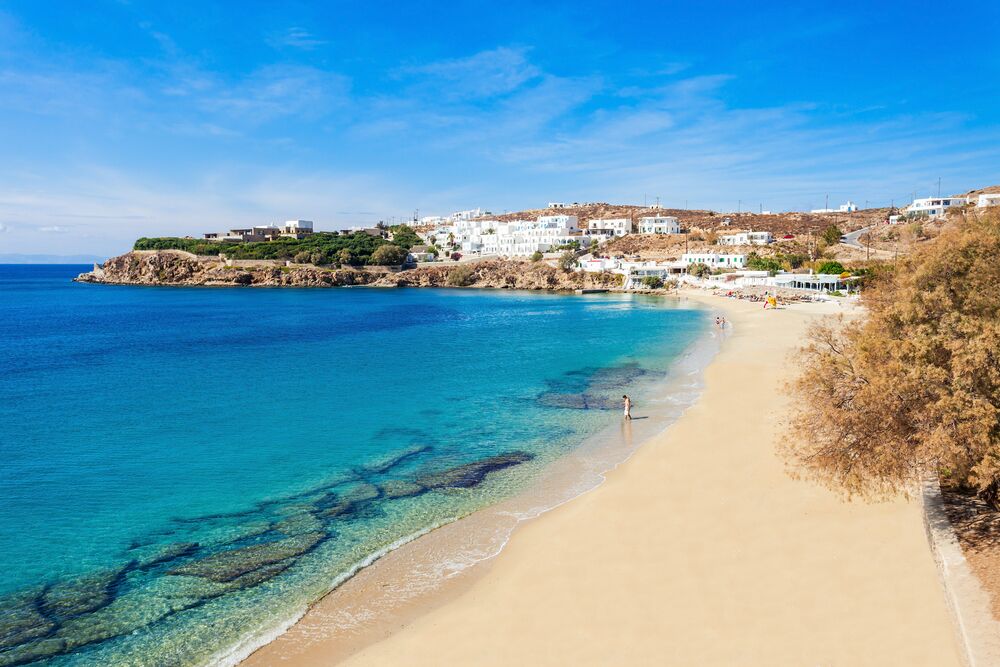 A coastal town with white buildings, a sandy beach, and clear blue waters.