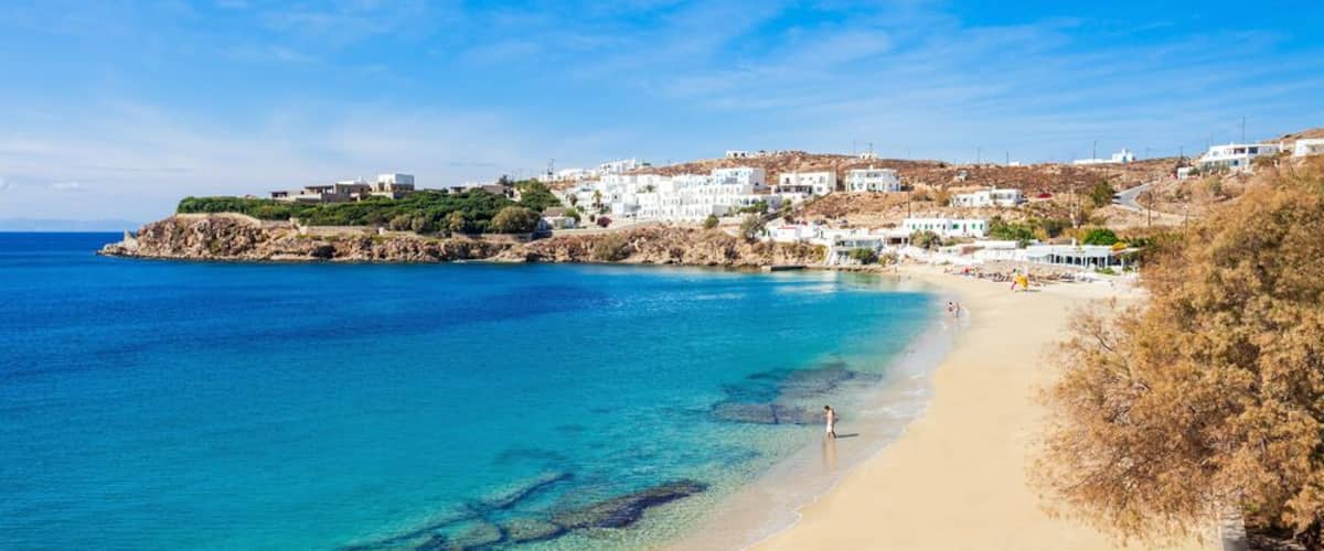 A coastal town with white buildings, a sandy beach, and clear blue waters.