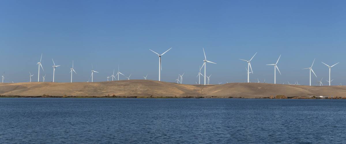 A landscape with multiple wind turbines on a hill by a body of water.