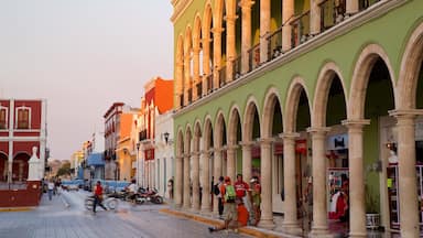 Una calle bordeada de edificios coloridos, incluyendo un edificio verde con arcos y uno rojo con balcones.