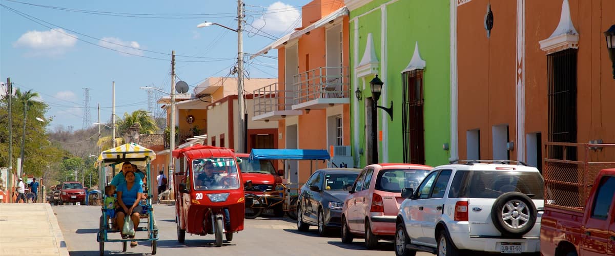 A busy street with colorful buildings, parked cars, and a tuk-tuk with passengers.