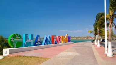 A coastal walkway with colorful letters spelling out a destination name, palm trees, and a clear blue sky.
