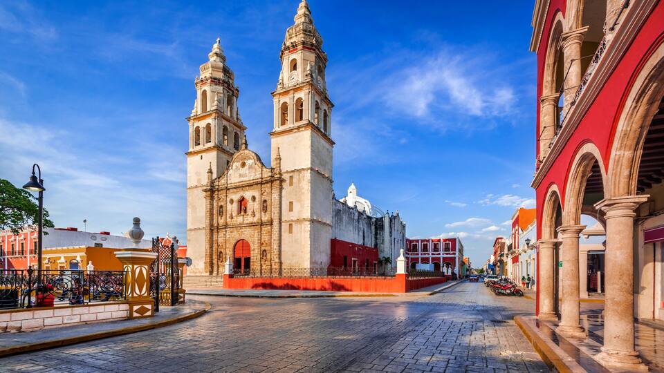 A historic church with two towers, a cobblestone street, and surrounding buildings.