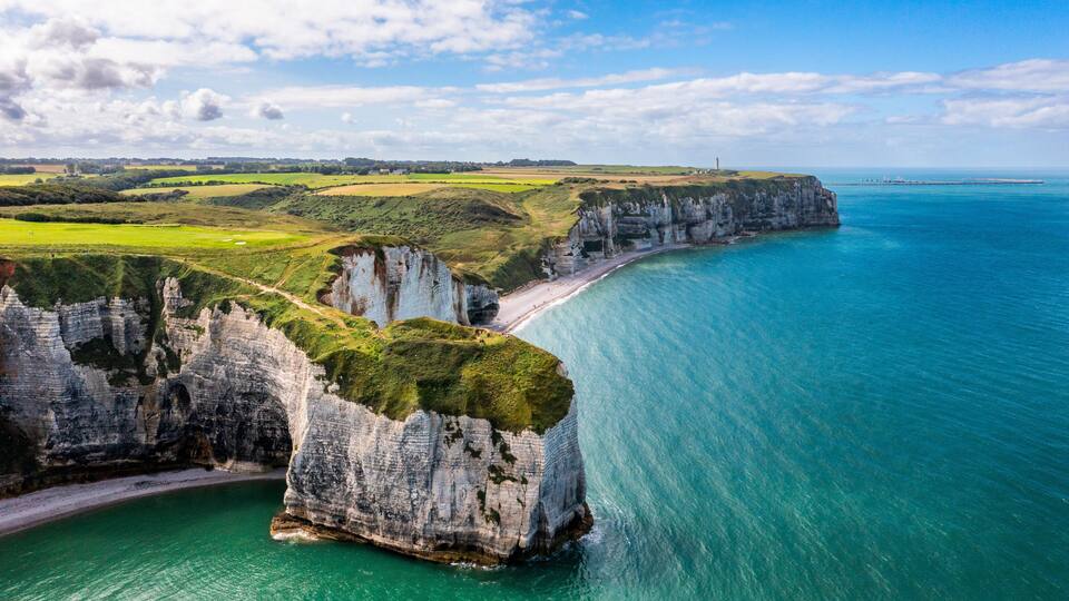 A coastal landscape with cliffs, a beach, and a lighthouse.