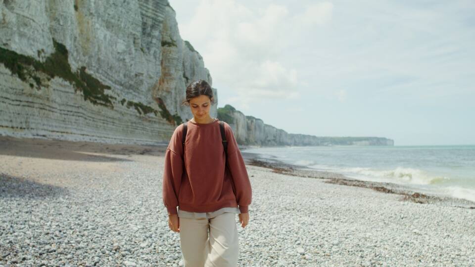 A person walking on a pebble beach with white cliffs in the background.