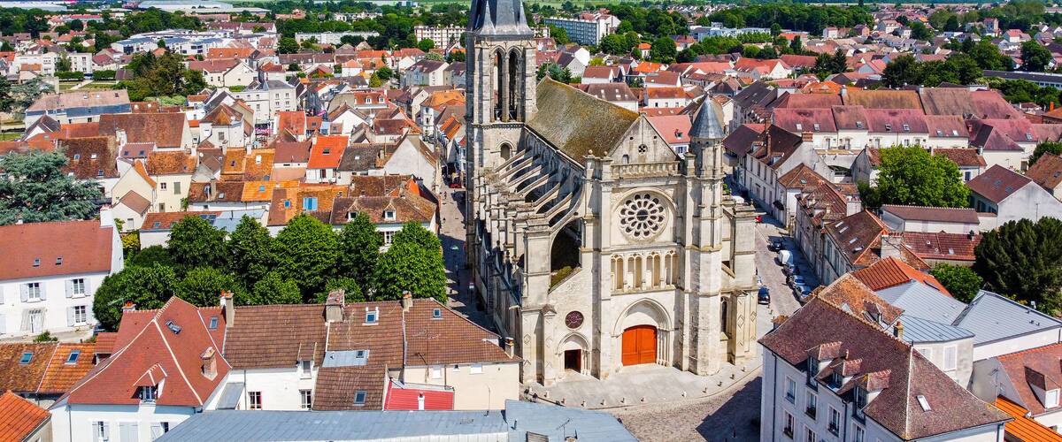 A cathedral with a tall spire and a rose window, surrounded by a densely packed town with red-roofed buildings.
