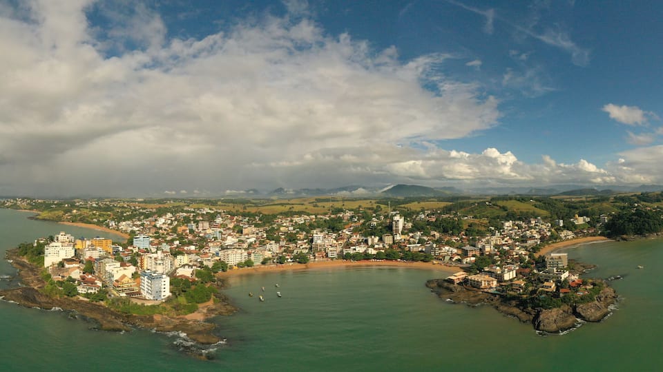 An aerial view of a coastal town with a bay, buildings, and a mountainous backdrop.