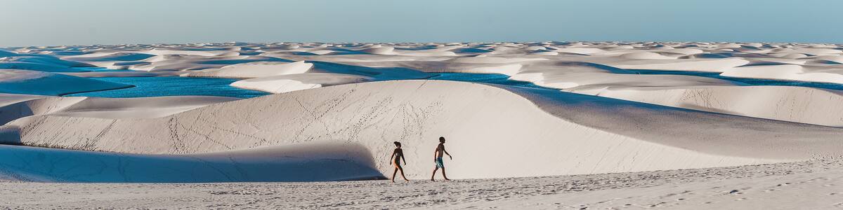travel couple trek across giant sand dunes with lagoons in Lencois Maranhenses, one of the most stunning tourist attractions in North-East Brazil