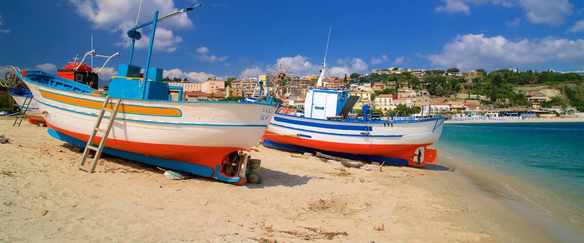 Two colorful boats on a sandy beach with a clear blue sky and a coastal town in the background.