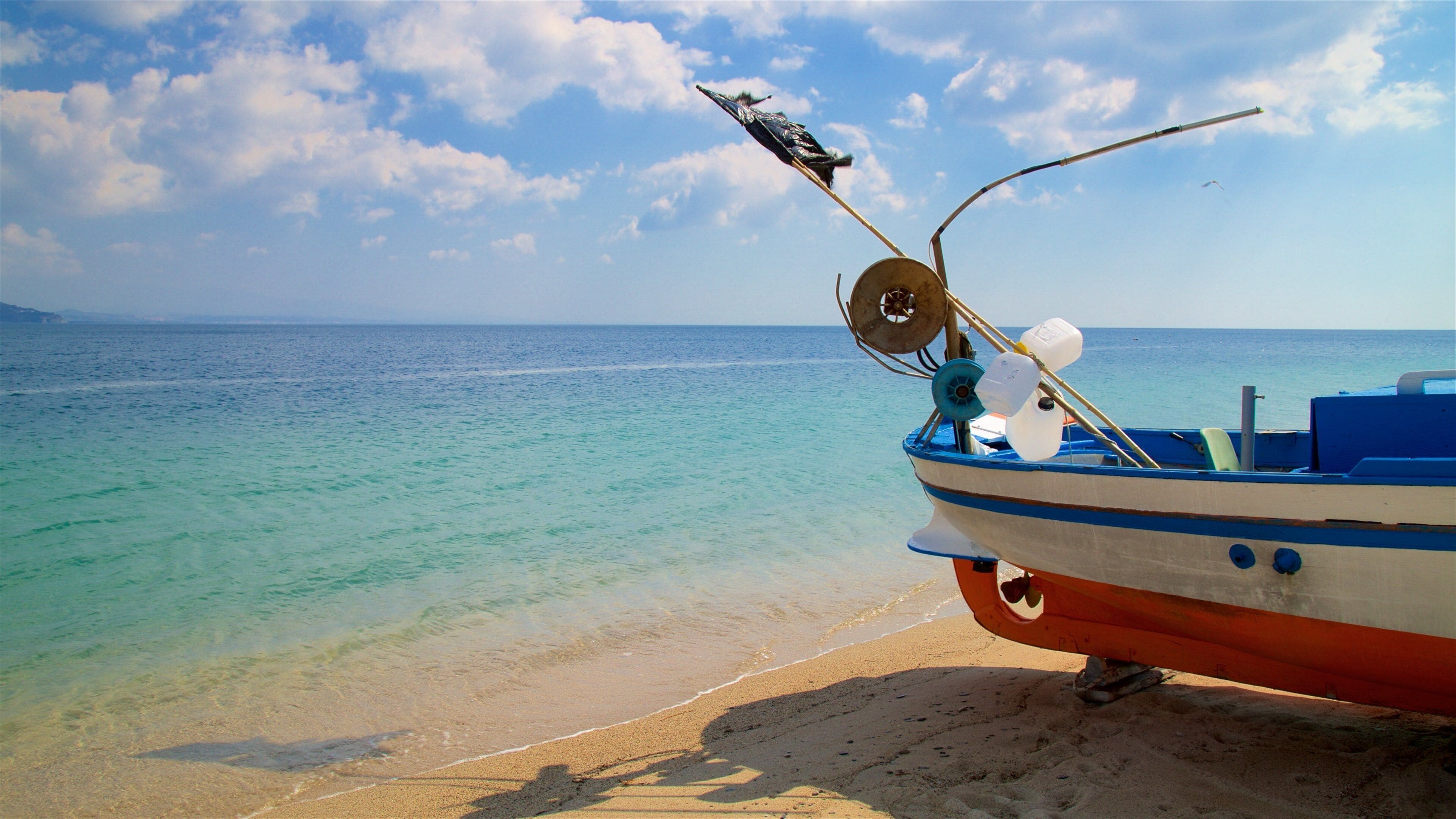 A boat with a fishing rod and reel on a sandy beach by the sea.
