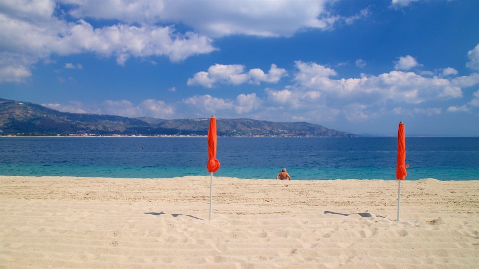 Une plage avec deux parasols orange, une personne dans l’eau et une chaîne de montagnes en arrière-plan.