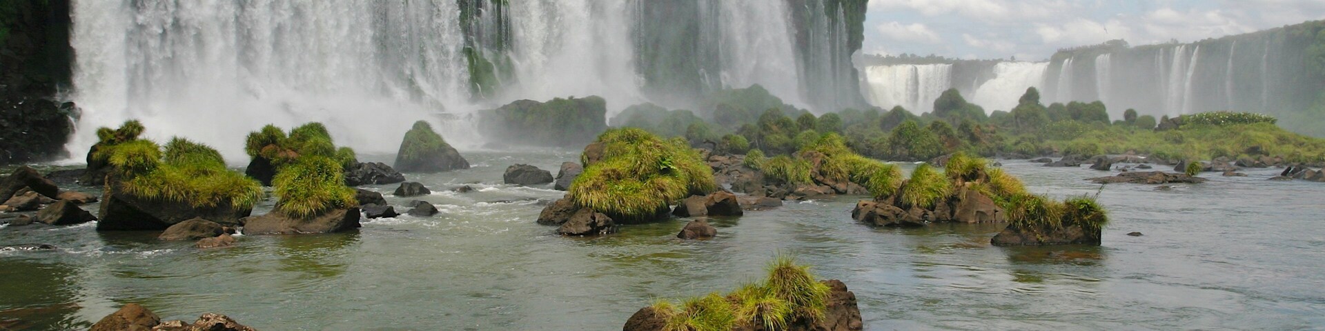 Una cascada grande se precipita sobre rocas con abundante vegetación al frente.