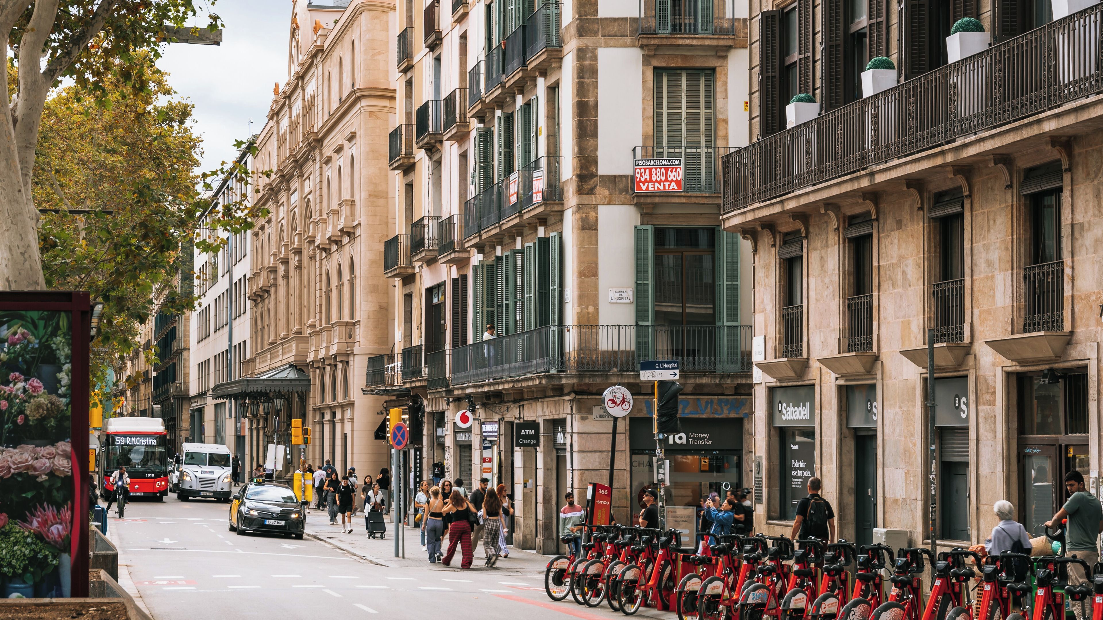 Uma rua urbana movimentada com edifícios históricos, uma placa de hospital e uma fileira de bicicletas vermelhas.