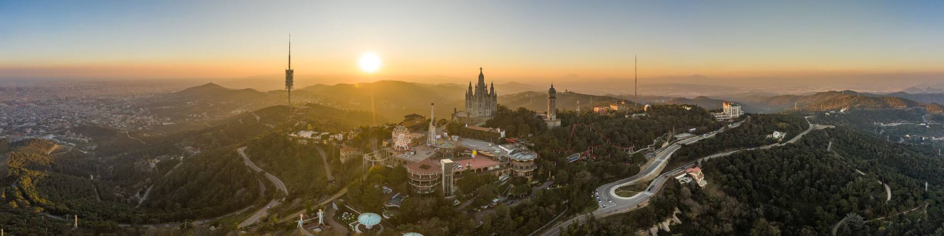 A panoramic view of a city with a prominent cathedral, a Ferris wheel, and winding roads amidst a hilly landscape.