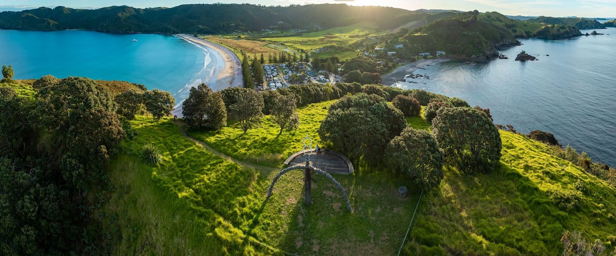 A coastal landscape with a beach, grassy hills, and a clear blue sea.
