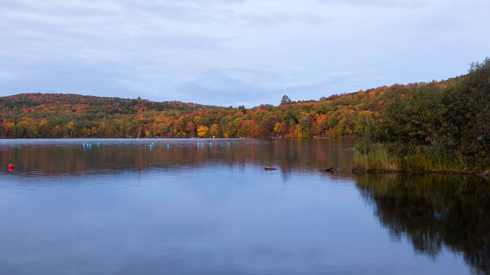 A calm lake surrounded by autumn-colored trees and a hilly landscape.