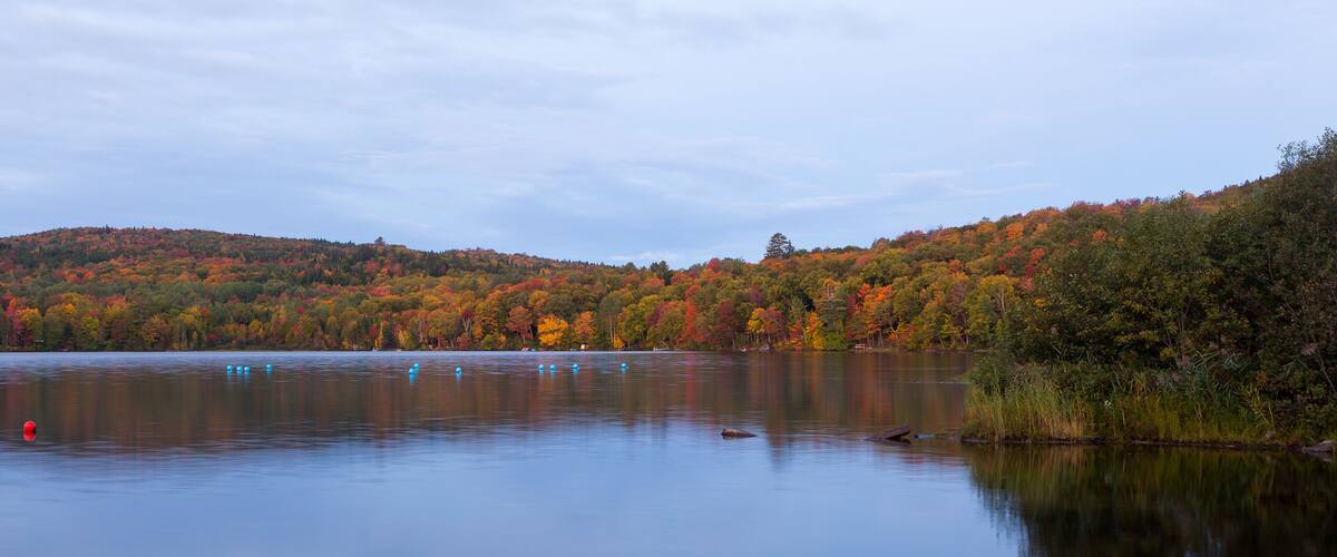 The Delage lake seen at dawn during the Fall season, with colourful wooded mountains in the background, Lac-Delage, Quebec, Canada