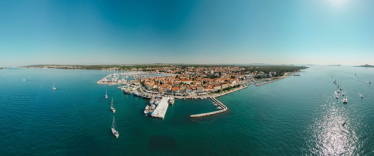 An aerial view of a coastal town with a marina, boats, and a clear blue sky.