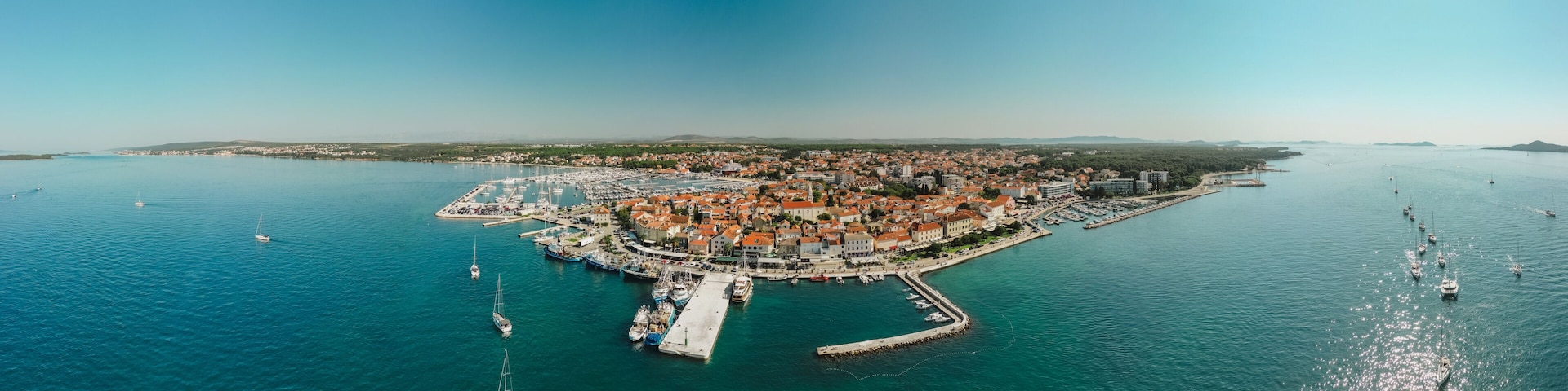An aerial view of a coastal town with a marina, boats, and a clear blue sky.