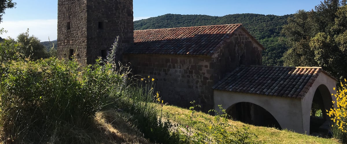 A stone tower with a tiled roof, a small building with a tiled roof, and an arched bridge in a hilly landscape.