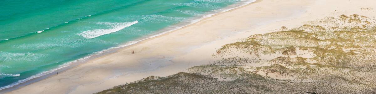 A coastal landscape with a sandy beach and a clear blue ocean.