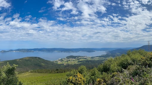 A stunning photo of Ria de Muros e Noia, Galicia, showcasing vast water, lush green hills, and quaint coastal towns. Fluffy clouds add drama to the serene landscape.